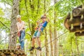 Mother and son climbing in extreme road trolley zipline in forest on carabiner safety link on tree to tree top rope