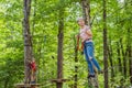 Mother and son climbing in extreme road trolley zipline in forest on carabiner safety link on tree to tree top rope