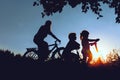 Mother with son and daughter riding bikes and scooter at sunset