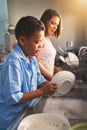 Mother, son and dishes in kitchen with help or teamwork, tasks with collaboration in home. Woman, boy and cleaning plate Royalty Free Stock Photo