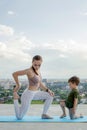 Mother and son doing exercise on the balcony in the background of a city during sunrise or sunset, concept of a healthy lifestyle Royalty Free Stock Photo