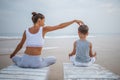 A mother and a son are doing yoga exercises at the seashore of tropic ocean Royalty Free Stock Photo