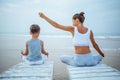A mother and a son are doing yoga exercises at the seashore of tropic ocean Royalty Free Stock Photo