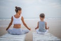 A mother and a son are doing yoga exercises at the seashore of tropic ocean Royalty Free Stock Photo