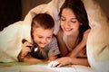 Mother and son with flashlight reading book under blanket Royalty Free Stock Photo