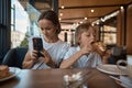 Mother and son having lunch in sidewalk restaurant. Mom and son eat a croissant in a cafe. Woman photographing food Royalty Free Stock Photo