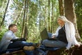 Mother and son with a laptops in forest in summer. Fat young smart teenage boy and woman working with modern IT Royalty Free Stock Photo