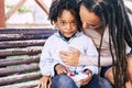 Mother and son love - childhood family concept with black race kid and mommy with dreads together hug and have fun at the park - Royalty Free Stock Photo