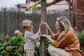 Mother with son making bug hotel, or insect house outdoors in the garden. Boy learning about insects, garden ecosystem