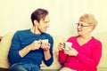 Mother and son sitting on couch and drinking tea or coffee