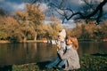 Mother and son sitting near lake in autumn park on sunset and looking away. Family having fun, hugging, laughing, relaxing, enjoy Royalty Free Stock Photo