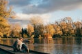 Mother and son sitting near lake in autumn park on sunset and looking away. Family having fun, hugging, laughing, relaxing, enjoy Royalty Free Stock Photo