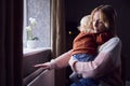 Mother With Son Trying To Keep Warm By Radiator At Home During Cost Of Living Energy Crisis