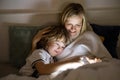 Mother and son using digital tablet together at night in bed Royalty Free Stock Photo