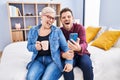 Mother and son using smartphone drinking coffee sitting on bed at bedroom Royalty Free Stock Photo