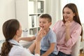 Mother and son visiting pediatrician. Doctor examining patient`s throat in hospital Royalty Free Stock Photo