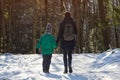 Mother with son walking along snow-covered road against the background of coniferous forest. Winter sunny day. Close-up Royalty Free Stock Photo