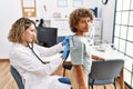 Mother and son wearing doctor uniform auscultating child back at clinic