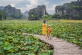 Mother and son in a yellow on the path among the lotus lake. Mua Cave, Ninh Binh, Vietnam. Vietnam reopens after