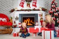 Merry Christmas and Happy Holidays!Mother and sons sitting by the fireplace and open Christmas gifts from Santa.