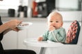 Mother spoon feeding her baby boy child in baby chair with fruit puree in kitchen at home. Baby solid food introduction Royalty Free Stock Photo
