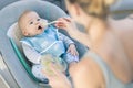 Mother spoon feeding her baby boy infant child in baby chair with fruit puree. Baby solid food introduction concept. Royalty Free Stock Photo