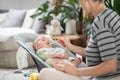 Mother spoon feeding her baby boy infant child in baby chair with fruit puree. Baby solid food introduction concept. Royalty Free Stock Photo