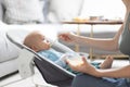 Mother spoon feeding her baby boy infant child in baby chair with fruit puree. Baby solid food introduction concept. Royalty Free Stock Photo