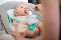 Mother spoon feeding her baby boy infant child in baby chair with fruit puree. Baby solid food introduction concept. Royalty Free Stock Photo