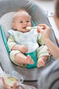 Mother spoon feeding her baby boy infant child in baby chair with fruit puree. Baby solid food introduction concept. Royalty Free Stock Photo