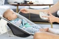 Mother spoon feeding her baby boy infant child in baby chair with fruit puree. Baby solid food introduction concept. Royalty Free Stock Photo