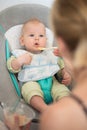 Mother spoon feeding her baby boy infant child in baby chair with fruit puree. Baby solid food introduction concept. Royalty Free Stock Photo