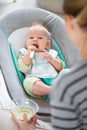 Mother spoon feeding her baby boy infant child in baby chair with fruit puree. Baby solid food introduction concept. Royalty Free Stock Photo