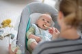 Mother spoon feeding her baby boy infant child in baby chair with fruit puree. Baby solid food introduction concept. Royalty Free Stock Photo