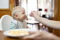 Mother spoon feeding her infant baby boy child sitting in high chair at the dining table in kitchen at home Royalty Free Stock Photo