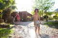 Mother sprays a child with a hose in the courtyard of the house, Boy drenched in water on a hot sunny day