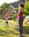 Mother sprays a child with a hose in the courtyard of the house, Boy drenched in water on a hot sunny day