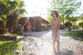 Mother sprays a child with a hose in the courtyard of the house, Boy drenched in water on a hot sunny day