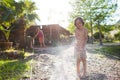 Mother sprays a child with a hose in the courtyard of the house, Boy drenched in water on a hot sunny day