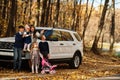 Mother stand near white suv car with four kids in autumn park. Family walk in fall forest Royalty Free Stock Photo