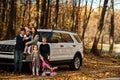 Mother stand near white suv car with four kids in autumn park. Family walk in fall forest Royalty Free Stock Photo