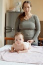 Mother stands next to the child. Massage for the baby. Four month old baby smiling doing gymnastics Royalty Free Stock Photo