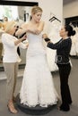 Mother and store employee assisting young woman getting dressed in bridal store