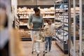 Mother in supermarket shopping for groceries with little girl and pushing cart Royalty Free Stock Photo