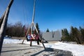 Mother swinging with daughters in big wooden swing in early spring snowy mountains against tiny house and car Royalty Free Stock Photo