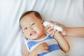 Mother takes temperature for baby boy with ear thermometer on bed at home Royalty Free Stock Photo
