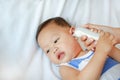 Mother takes temperature for baby boy with ear thermometer on bed at home Royalty Free Stock Photo