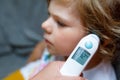 Mother takes temperature for her little preschool daughter, sick child with infrared in ear thermometer at home, high Royalty Free Stock Photo