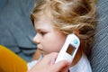 Mother takes temperature for her little preschool daughter, sick child with infrared in ear thermometer at home, high Royalty Free Stock Photo