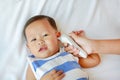 Mother takes temperature for infant with ear thermometer on bed at home Royalty Free Stock Photo